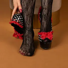 Feet in black lace stockings with red and black high heels, one worn and the other held in her hand - Foot Fetish Zurich