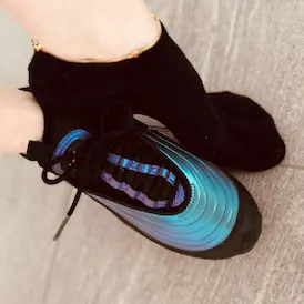 Lady Samantha's feet, one in a black sock with an anklet, the other in a shiny, metallic-blue sneaker - Foot Fetish Zurich